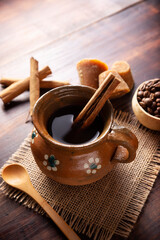 Authentic homemade mexican coffee (cafe de olla) served in traditional handmade clay mug (Jarrito de barro) on rustic wooden table.