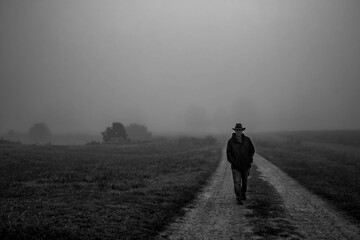 A moody vibe as a man saunters along a dirt road towards the viewer on a calm foggy morning.