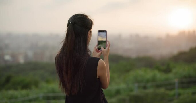 Woman take photo on cellphone under sunset