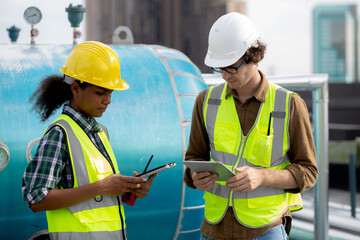 Young woman and man engineer examining pipeline and looking digital tablet in the factory, mechanic or technician inspector plumber valve and talking together, industrial and maintenance concept.
