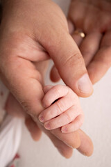 The hand of a sleeping newborn in the hand of parents, mother and father close-up. Tiny fingers of a newborn. The family is holding hands. Studio macro photography. Concepts of family and love.