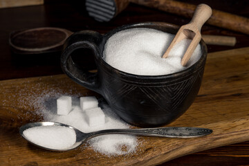 White sugar in a sugar bowl standing on a wooden kitchen table. White sugar in cubes and crystals, poured on a wooden kitchen board.
