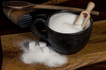 White sugar in a sugar bowl standing on a wooden kitchen table. White sugar in cubes and crystals, poured on a wooden kitchen board.