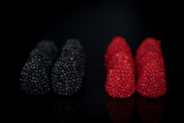 fruit gummies in the shape of raspberries and blackberries, arranged in rows next to each other.
black reflective background