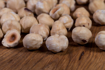 Hazelnut - edible fruit of various species of shrubs of the genus hazel (Corylus). Roasted hazelnuts. Whole hazelnuts and walnut halves, scattered on a wooden board.