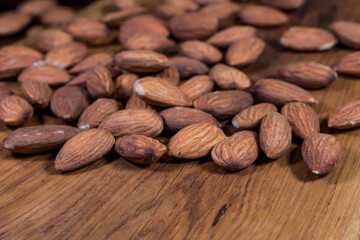 Whole almonds, scattered on a wooden board. Almond fruit seeds. Edible raw, and suitable for preserves. Almonds are a valuable source of micro and macro elements and monounsaturated fatty acids.