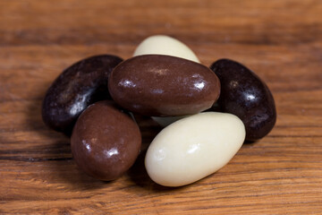 Three types of chocolate-coated almonds; dark chocolate, milk chocolate, white chocolate. High-quality sweets in Belgian chocolate. Sweets arranged on a wooden board. Blurred background.