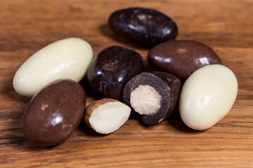 Fototapeta na wymiar Three types of chocolate-coated almonds; dark chocolate, milk chocolate, white chocolate. High-quality sweets in Belgian chocolate. Sweets arranged on wooden board. Blurred background. Visible center.