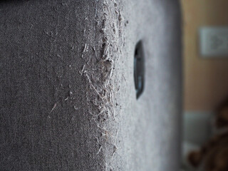 A gray sofa filled with cat scratch marks on the edge of the sofa.