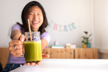 Happy teen asian female student showing healthy green juice at camera. Focus on juice. Copy space. Healthy lifestyle