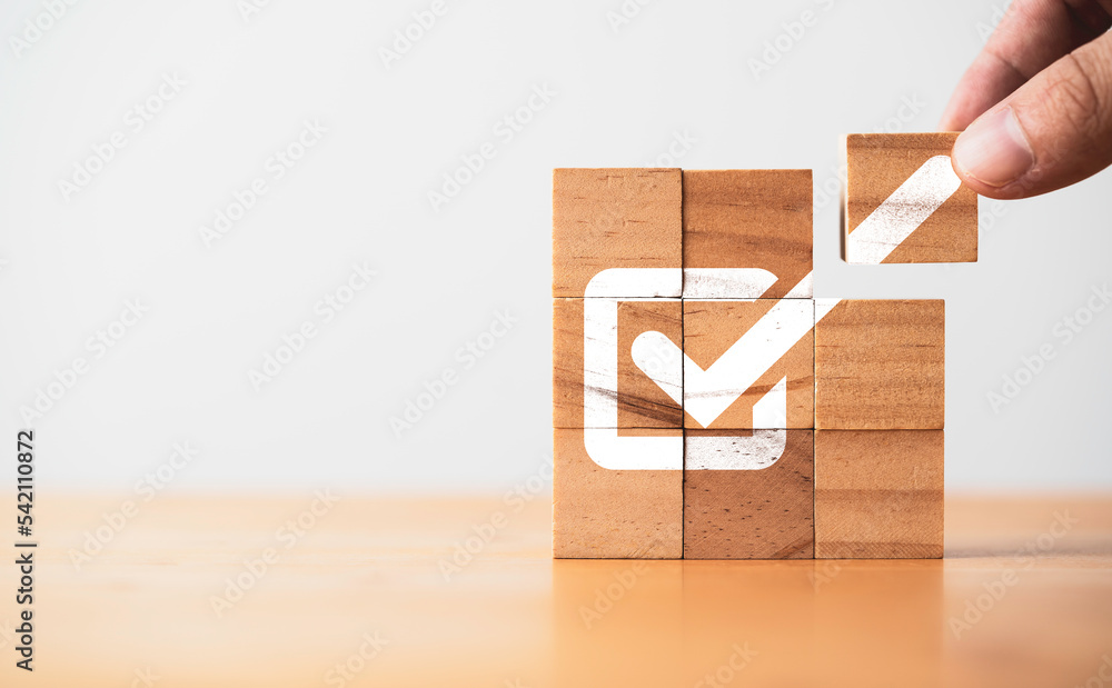 Poster Hand assemble correct tick sign mark on wooden block cube for document approve business project and quality assurance concept.