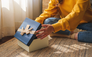 Closeup image of a young woman receiving and opening a gift box at home