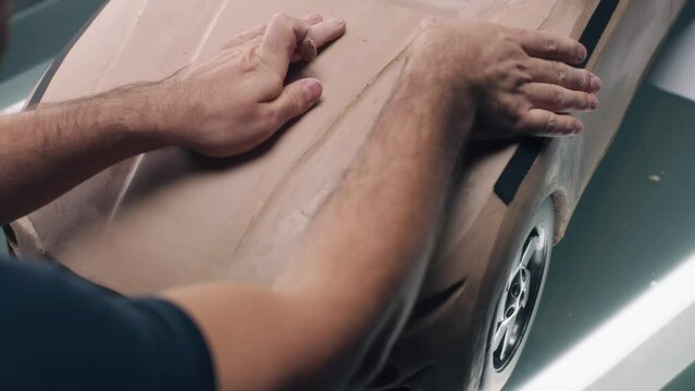 High angle shot of male automotive designer sculpting futuristic car model from plasticine clay. Future design of new generation electric car. Working in modern car design studio.