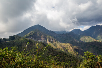 Fototapeta premium Rainclouds brush lush forest mountains with sunshine near Lake Atitlan, Guatemala.