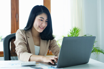 Portrait of a thoughtful Asian businesswoman looking at financial statements and making marketing plans using a computer on her desk