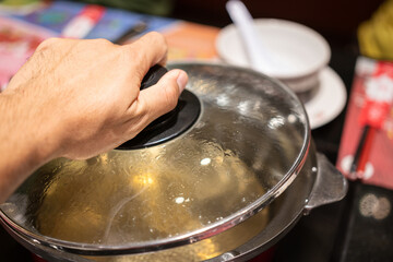 Action of people hand is preparing to open the Sukiyaki or Shabu Shabu pottery's lid after water already boiled. Selective focus photo.