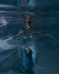 fashionable girl in a beautiful white dress under water in blue light and fluttering fabric in the depths