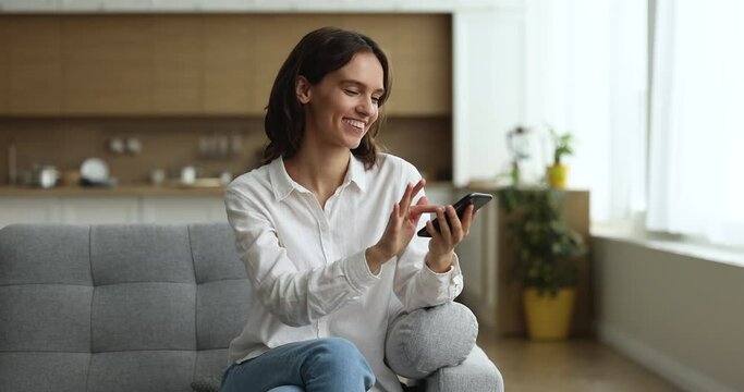 Woman sit on sofa holds smartphone search information on internet using virtual assistant and voice recognition, talk to friend on speaker phone smile enjoy modern tech usage for comfort life concept