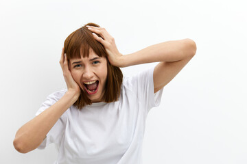 a funny, emotional woman stands on a light background in a T-shirt and holds her head with her hands while expressing emotions. Horizontal photo with an empty space for inserting an advertising layout