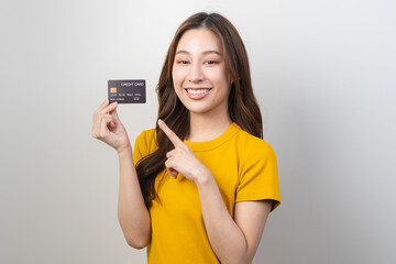 Portrait of smiling pretty brunette asian young woman, girl student in yellow casual hand holding, showing credit card  for buy, payment purchase to shopping, copy space isolated white background