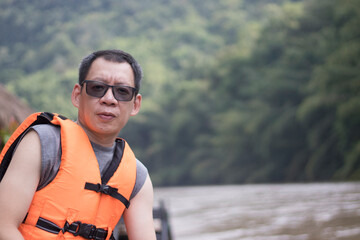 A man wearing a life jacket while waiting to swim, looking at the camera sitting on a raft by the...