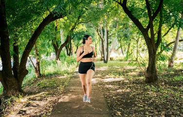 Healthy lifestyle concept of a woman jogging in a green park, Sporty young woman running in a park. Girl running in a park while listening to music, Lifestyle of sporty woman running in a park