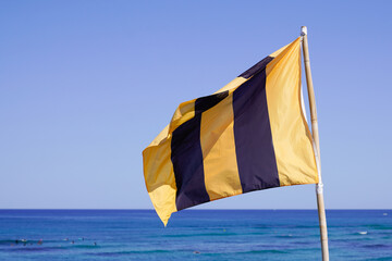 Warning flag yellow black vertical line blowing on the beach on sunny day