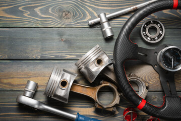 Sport car steering wheel, engine pistons and wrenches on the wooden workbench background with copy...