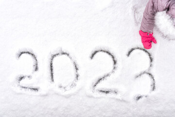 kid's hand writes 2023 on fresh snow. new year concept