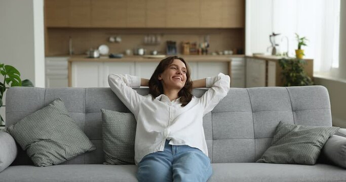 Peaceful woman relaxes alone on comfortable sofa in living room, put hands behind head, enjoy fresh air inside modern, smart home. Homeowner spend leisure resting in cozy flat, climate control concept