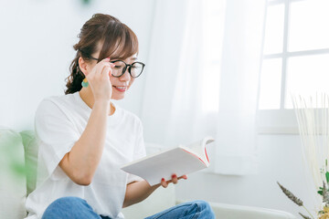メガネをかけて本を読むアジア人女性（読書）
