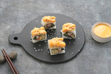 Sushi Rolls with crab stick, ebi, cucumber and mentai sauce served on chopping board
