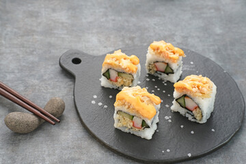 Sushi Rolls with crab stick, ebi, cucumber and mentai sauce served on chopping board
