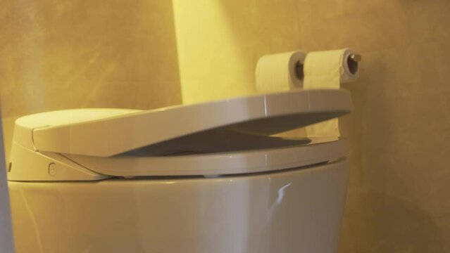 Automatic opening and closing the toilet. White toilet bowl with modern automatic soft opening mechanism of seat and woman in blue bathrobe sitting on toilet bowl in morning.  