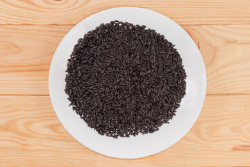 Raw black rice on dish on rustic table, top view