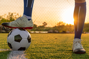 Athlete standing with ball on football field during sunrise, soccer ball in net on sky background, ball movement, popular sports on football club.