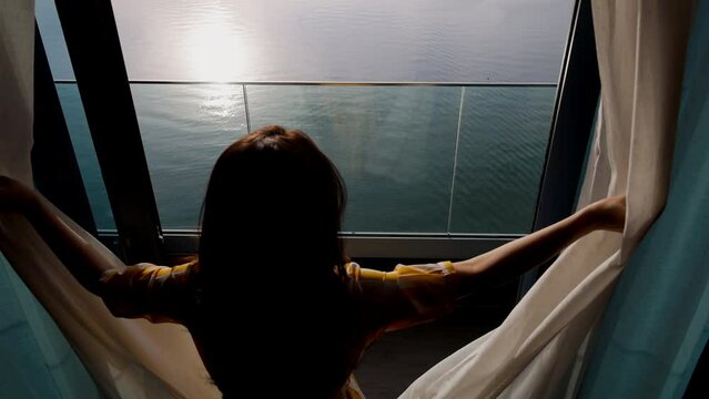 Resort vacation happy Asian woman tourist in yellow summer dress opening curtain and enjoying ocean view from balcony hotel room and Beautiful sunset above sea or ocean, reflection of sun in the water