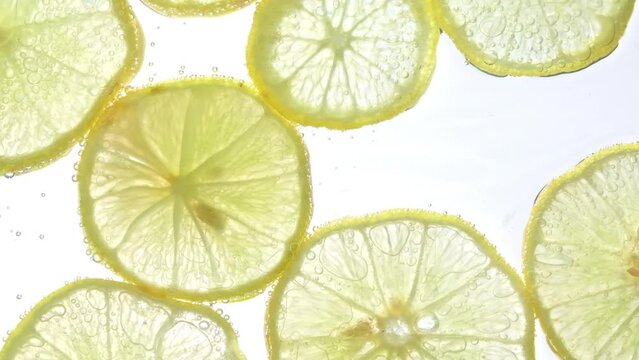 Juicy lemon slices with bubbles under water isolated on white background. Yellow lime slices pattern textured background.