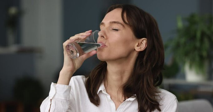 Close up shot attractive young woman holds glass drinks clear water, female enjoy clean mineral aqua for body refreshment at home. Keep healthy lifestyle, good life habit, natural hydration concept