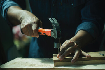 A carpenter furniture maker hammers a nail into the back of the cabinet with a hammer