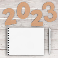 Cardstock Numbers 2023 Happy New Year Sign near White Spiral Paper Cover Notebook with Pen over table. 3d Rendering