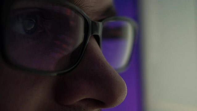 A programmer, a man in front of a computer, the code is reflected in the glasses. Working in IT, learning programming languages, developing applications and software.