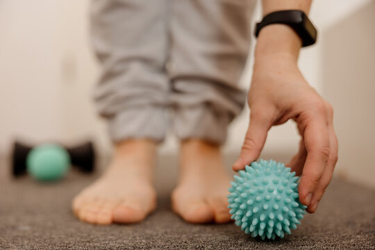 Woman doing flatfoot correction gymnastic exercise using massage ball. Myofascial relaxation of foot muscles. Hallux valgus. Pain. Identification of flat feet. Self care practices at home, healthcare.