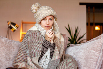 Woman warmly clothed and hat in a cold home sitting on couch