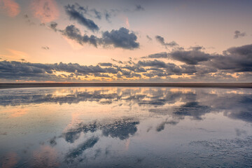 Colorful sunset with dark evening clouds reflecting in ripple-free sea water