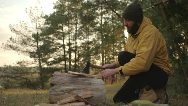 A survivalist chops wood for a nighttime bonfire.