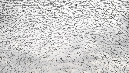 Broken glass, many cracks on glass transparent surface of window against cloudy gray sky. Texture background