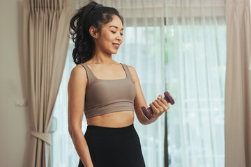 Fototapeta na wymiar Asian woman exercise at home. Young healthy female in sportswear workout training with dumbbell in living room, Health care and wellness concept.