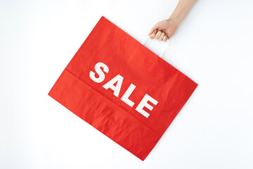 Hand holding red craft shopping bag with sign SALE. Minimal Black Friday shopping, sale, promotion advertising concept