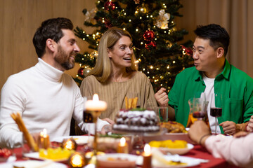 Friends celebrate Christmas eve or New Year holiday paty together sitting at the table. Feast at home group of multi ethnic festive christmas dinner. happy cheerful people.